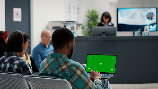 医院候诊室的年轻人在笔记本电脑上拿着绿屏