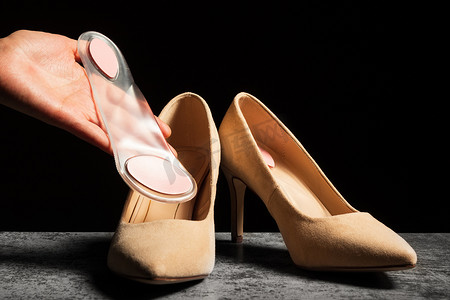 双足摄影照片_女人的手拿着柔软的矫形硅胶鞋垫，旁边是一双经典的高跟鞋