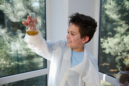 穿着白大褂的快乐调皮聪明的小学生，检查平底烧瓶中发生的化学反应