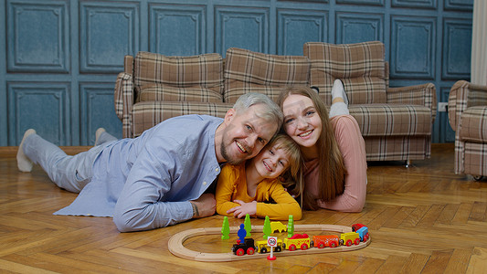 母亲、父亲和女儿的家人在家里的木制铁路上骑玩具火车