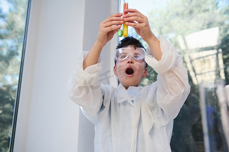 专注于一个穿着白色实验室外套和护目镜的小学生手中的试管，观察发生的化学反应