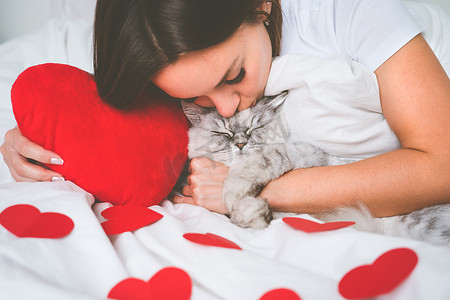 女人躺在床上，带着红心，亲吻她可爱的猫。