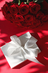 豪华假日丝绸礼盒和红色背景的玫瑰花束、浪漫惊喜和鲜花作为生日或情人节礼物