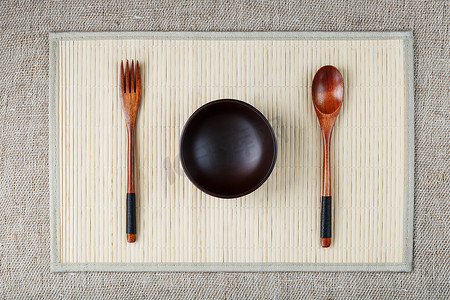 浅色竹背上用天然木材制成的空深色木杯、勺子和叉子