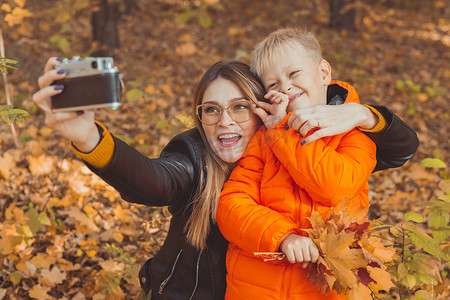 孩子和母亲摄影照片_儿子和母亲正在秋季公园里用相机自拍。