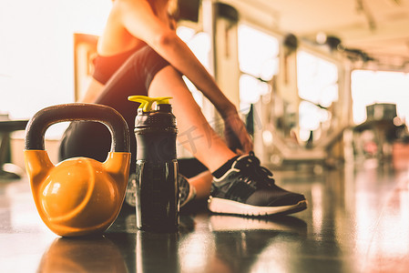 在蛋白质摇瓶背景的运动训练后，在健身房健身中用女性运动锻炼来关闭壶铃放松。