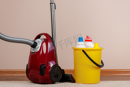 米色地毯上的红色吸尘器和带液体洗涤剂的塑料桶