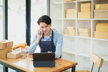 一家小型初创企业和中小企业主的肖像，一位亚洲男性企业家使用手机检查订单以整理产品，然后将它们包装到客户的内盒中