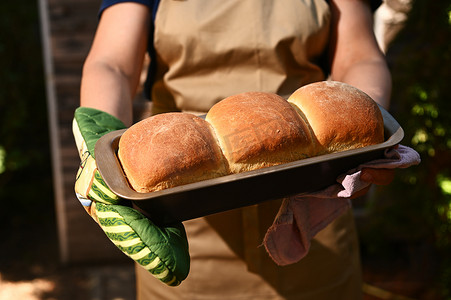 一位家庭主妇拿着烘焙容器的裁剪图像，里面装有新鲜出炉的硬皮自制全麦面包