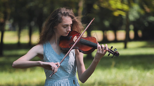 一个年轻的女孩在城市公园拉小提琴。