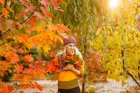 秋黄摄影照片_手拿秋叶、秋黄枫园背景的年轻女子