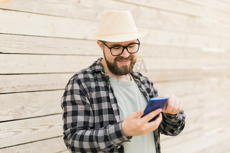 手机夏季夏季摄影照片_夏季城市突破木墙时，微笑的男性游客使用智能手机 — 技术和社交媒体应用概念