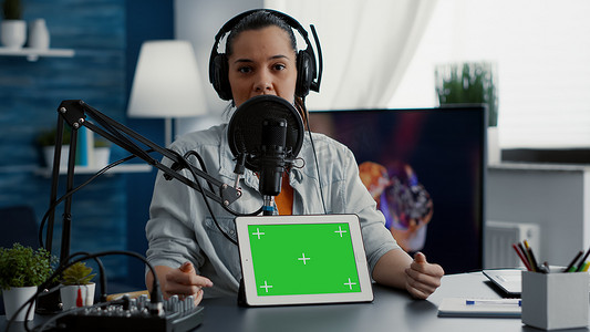 平板电脑绿幕摄影照片_工作室里的影响者在带有绿屏显示的平板电脑上推广产品。