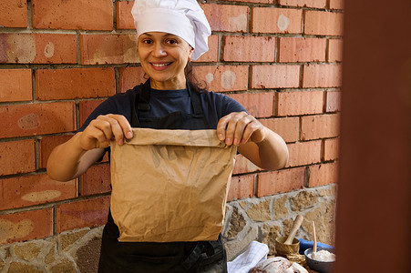 美女、面包店员工拿着一个纸袋，里面装着新鲜的传统面包，对着镜头微笑