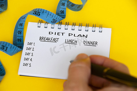 白色记事本上的饮食计划，黄色背景上有蓝色卷尺。