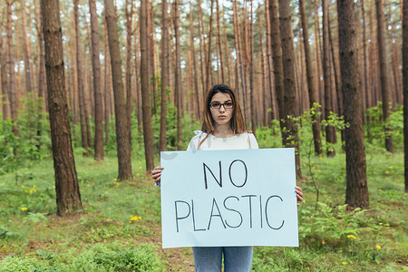 斗争摄影照片_年轻女活动家站在树林里，没有塑料海报，志愿者与森林污染作斗争