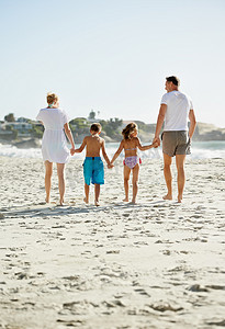 这对他们来说是美好的一天……一个快乐的年轻家庭在阳光下一起沿着海滩散步。