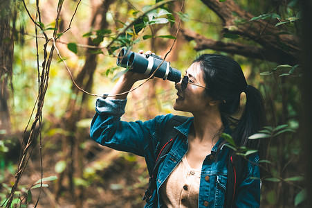 人望远镜摄影照片_美丽的亚洲女人带着双筒望远镜在森林里寻找目的地。
