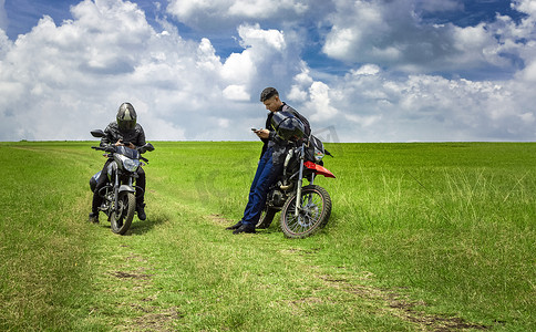 两个骑摩托车的男人停在田里聊天，两个年轻的摩托车手在田里，两个骑摩托车的男人在美丽的乡间小路上，年轻的摩托车手停在路上