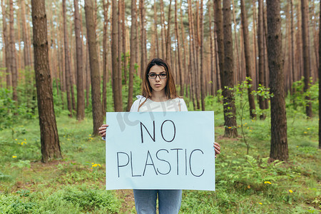 年轻女活动家站在树林里，没有塑料海报，志愿者与森林污染作斗争