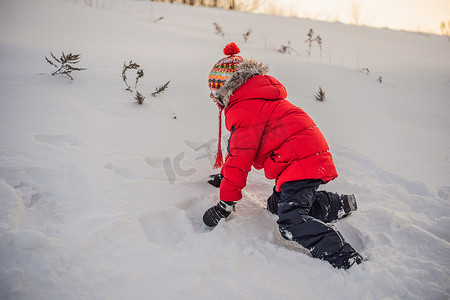 下雪玩耍摄影照片_穿着红色时装的男孩在户外玩耍。