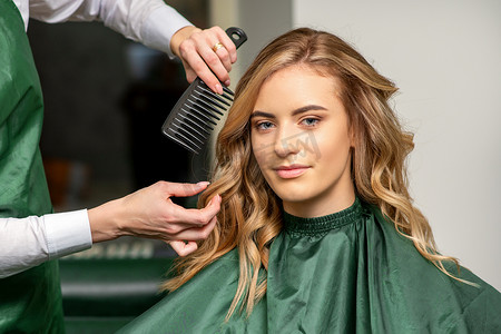 梳头发的人摄影照片_美发师一边用梳子梳头一边为女人做发型，在美发沙龙梳头。