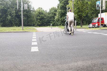 过马路摄影照片_男子驾着轮椅女子在人行横道过马路