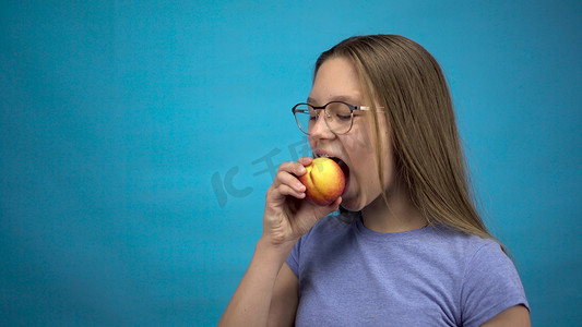 牙齿上戴着牙套的少女在蓝色背景下吃桃子。