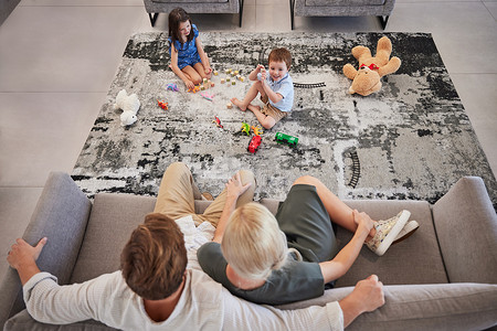 家庭、孩子和客厅，一个女孩和一个男孩在家里的地板上玩耍，而他们的父母则在沙发上放松。