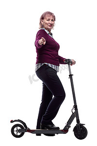 不忘初心砥砺前行摄影照片_微笑的老妇人骑着电动滑板车前行。