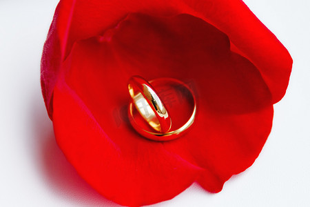 红色玫瑰花瓣上的金色结婚戒指。