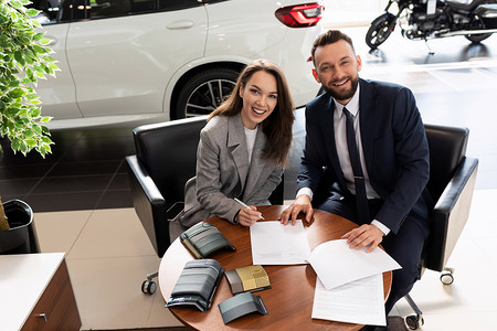 汽车经销店经理和满意的买家在经销店新车的背景下