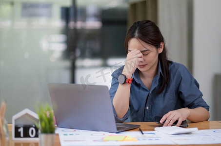 亚洲女性坐在家庭办公室里，承受着压力和眼睛疲劳。疲惫的女商人拿着眼镜，按摩鼻梁。