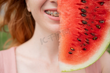 夏天，美丽的红发女人戴着牙套微笑，用一片西瓜遮住半张脸