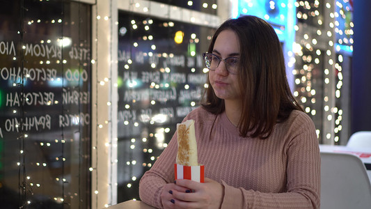 戴眼镜的年轻女子在一家餐馆吃卷饼。