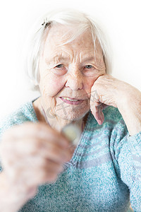 贫困老人摄影照片_快乐的 96 岁老妇人坐在家里的桌子旁，手里拿着一枚硬币，她很开心。