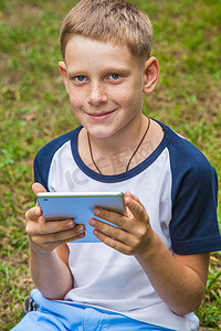 可爱的年轻白人小孩在公园里使用平板电脑。