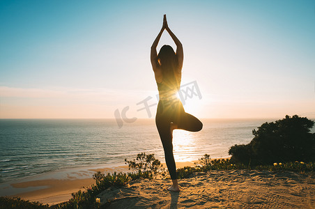 日落时分，女人在山上练习瑜伽和冥想，欣赏海景。