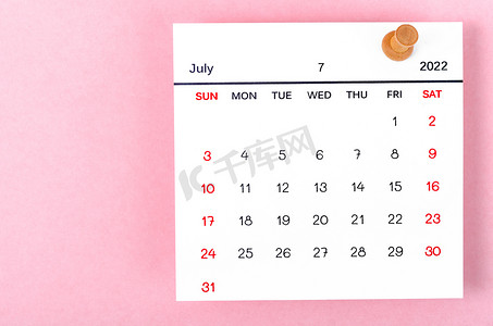 2022 年 7 月日历卡和粉红色背景的木制图钉。
