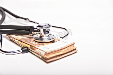 医疗保健成本概念形象：医疗图表上的听诊器和一堆钱，医疗保健成本或健康保险的象征，在白色背景下被隔离。