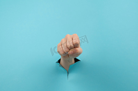 一个女人的手从蓝色背景的洞里伸出来，显示出一个拳头。