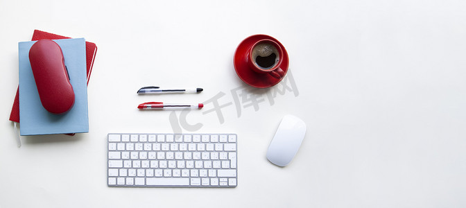 白眼镜盒摄影照片_带红黑笔的白色键盘和鼠标、咖啡杯、白桌上的笔记本
