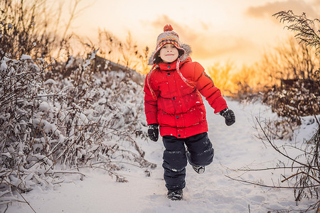 穿着红色冬装的可爱男孩在雪地里奔跑。