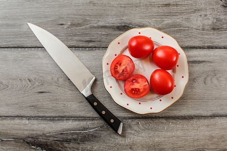 西红柿，其中一个在白色瓷盘上切成两半，上面有小红点，旁边放着厨师刀。