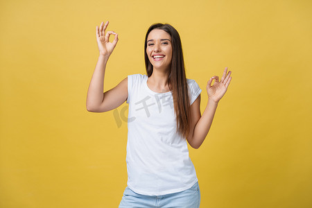 黄色手指手势摄影照片_黄色背景中，快乐的年轻女子用手指展示“ok”的手势