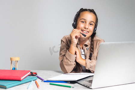 歌手写歌的作词摄影照片_戴耳机的微笑白人小女孩在家使用笔记本电脑在线手写学习，戴耳机的可爱快乐小孩参加互联网网络课程或电脑课堂，家庭教育概念