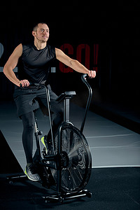 健身男性在功能训练馆使用空气自行车进行有氧运动。