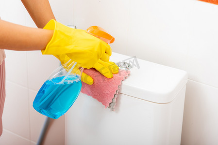 亚洲妇女用液体喷雾和粉红布擦拭家中厕所清洁马桶座圈的手