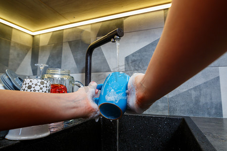 用海绵手在水下洗杯子，家庭主妇用蓝色海绵在厨房水槽里洗蓝色杯子，手清洁，手动，家务洗碗机
