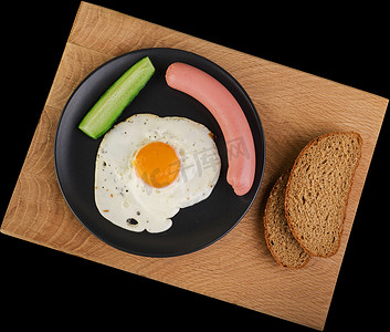 黑盘上的鸡蛋、香肠和黄瓜炒鸡蛋，黑色背景的木板上有两片面包